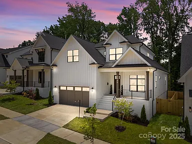 Modern white house with black roof and trim. Garage, front porch, and landscaped yard.