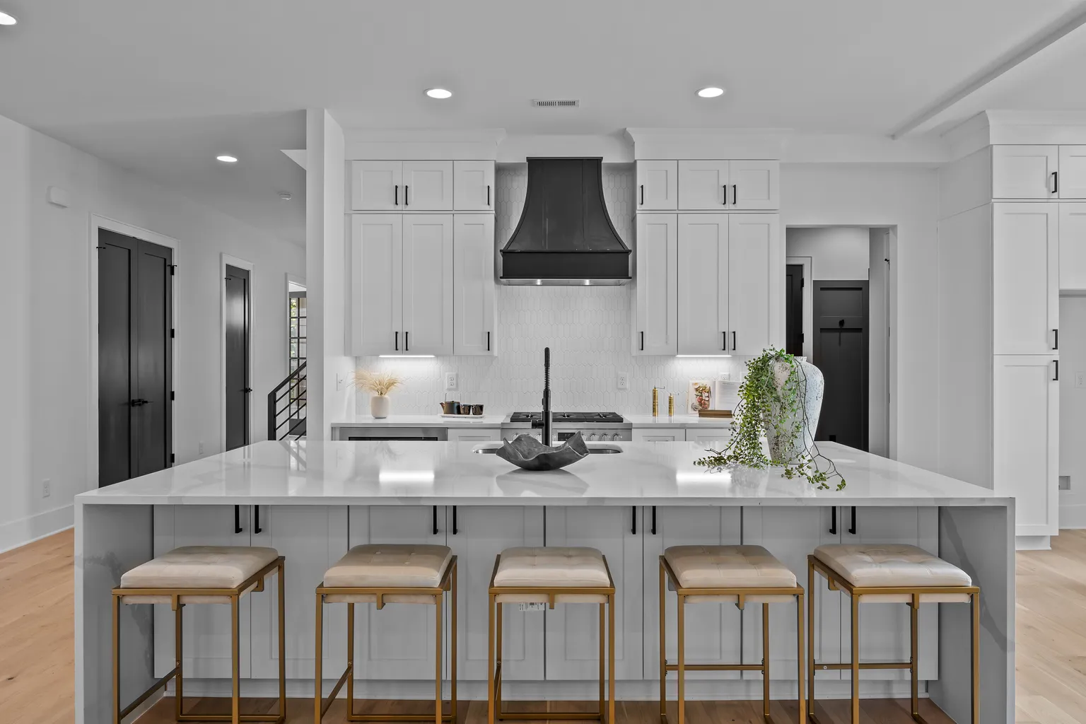 Modern kitchen with white cabinets, black range hood, large island with gold stools.