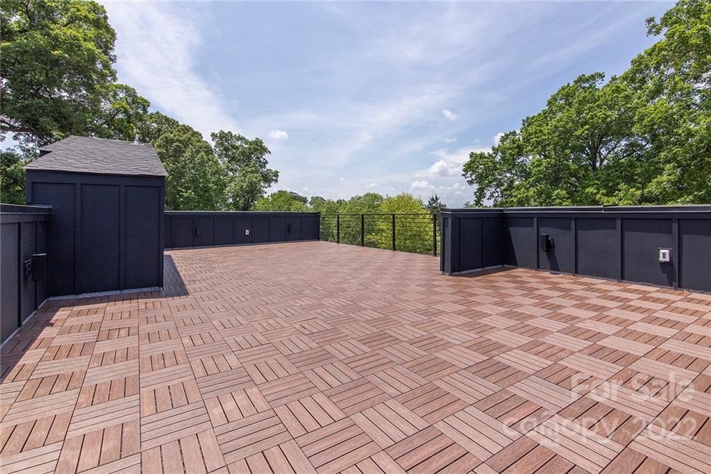 Rooftop deck with wood-like tiles, black walls, and trees against a blue sky.