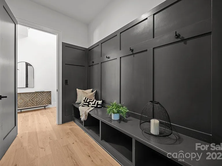 Entryway with dark gray paneling, bench, hooks, and open doorway to a room with a mirror and chest.