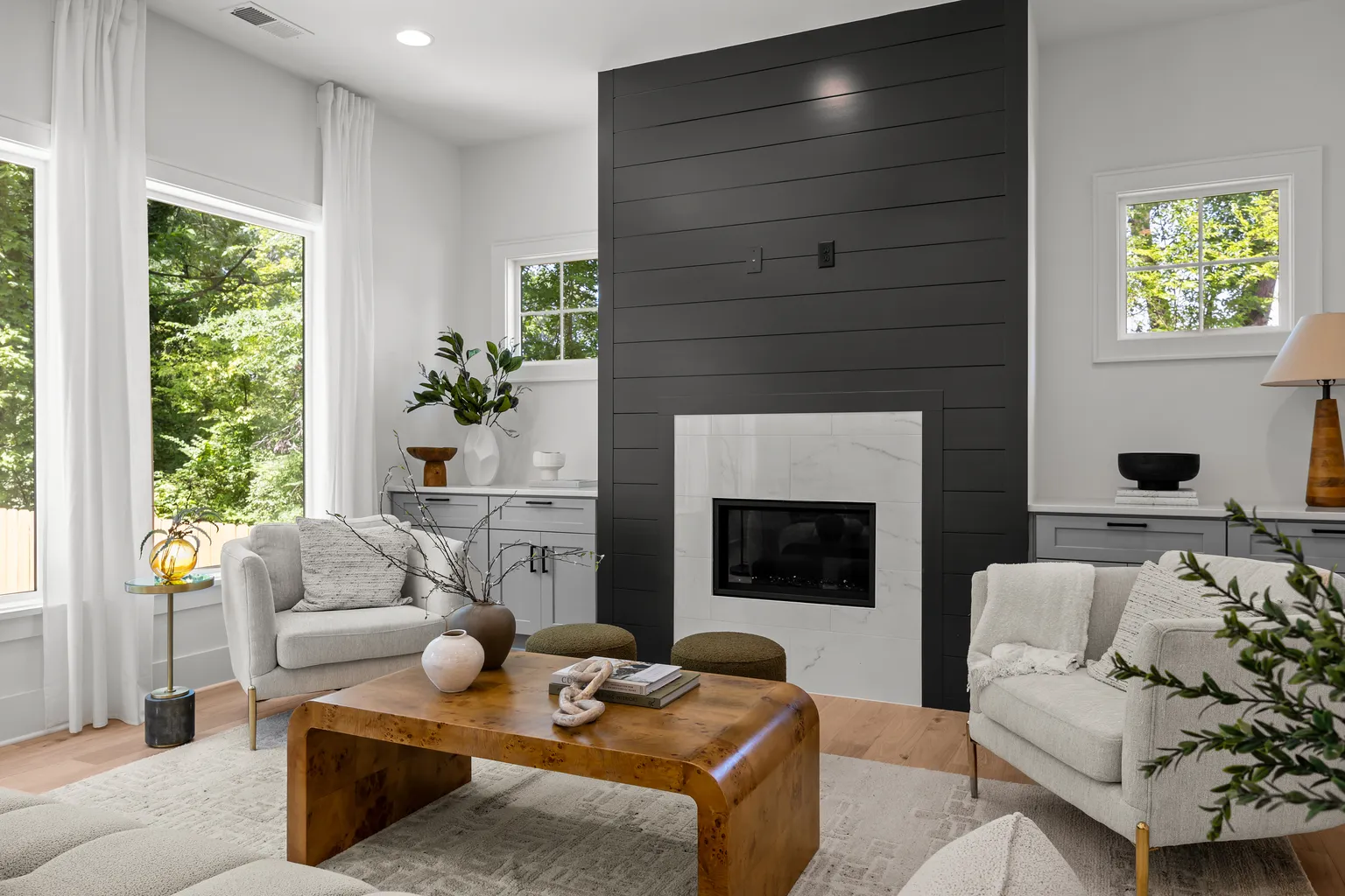 Living room with modern fireplace, neutral furniture, large windows, and wooden coffee table.