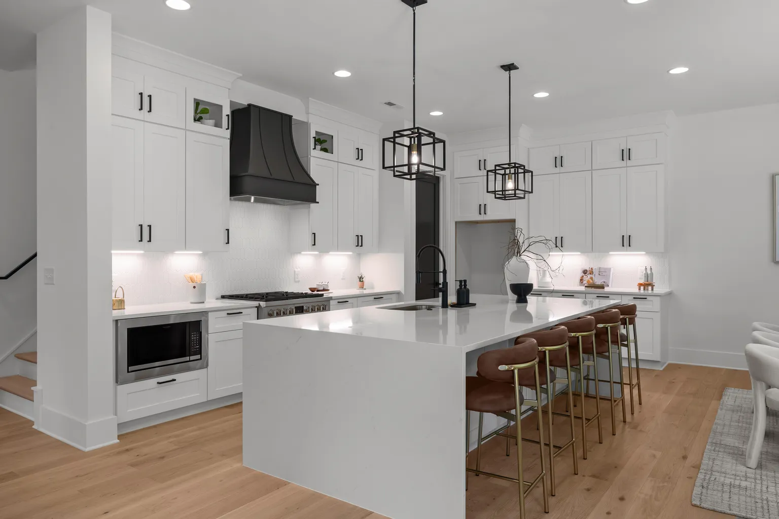 White kitchen with island, black accents, pendant lights, and wood flooring.