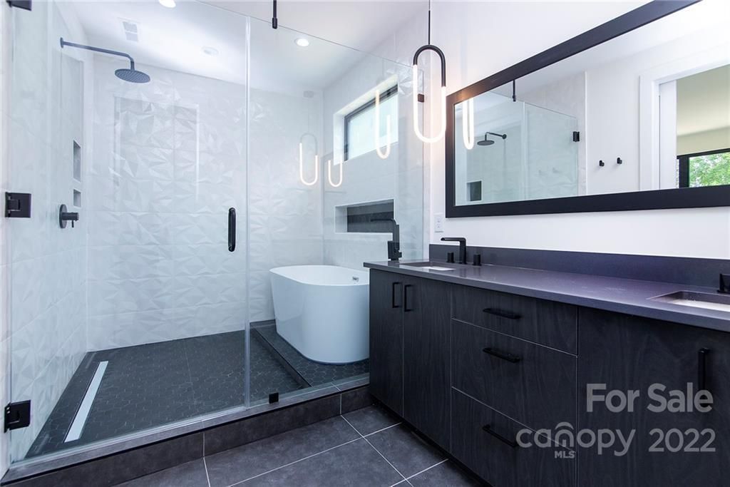Modern bathroom with a glass shower, dark vanity, and pendant lights.