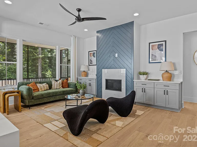 Living room with green couch, black chairs, fireplace, and forest view.