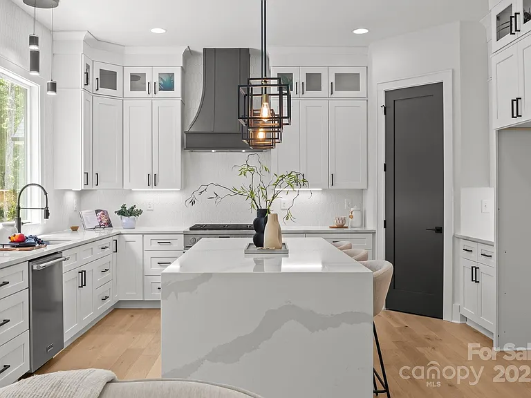 Modern white kitchen with island, stainless steel appliances, black accents, and light wood flooring.