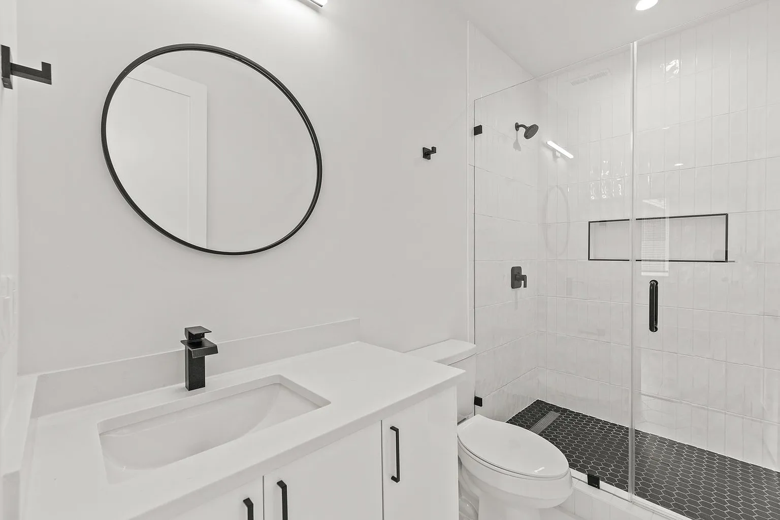 White bathroom with black accents: vanity, mirror, fixtures, shower, and toilet.