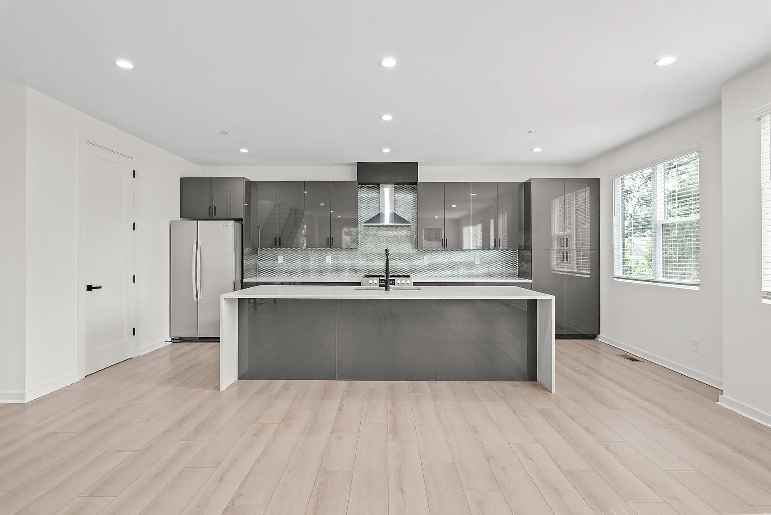 Modern gray and white kitchen with a large island, stainless steel appliances, and light wood floors.
