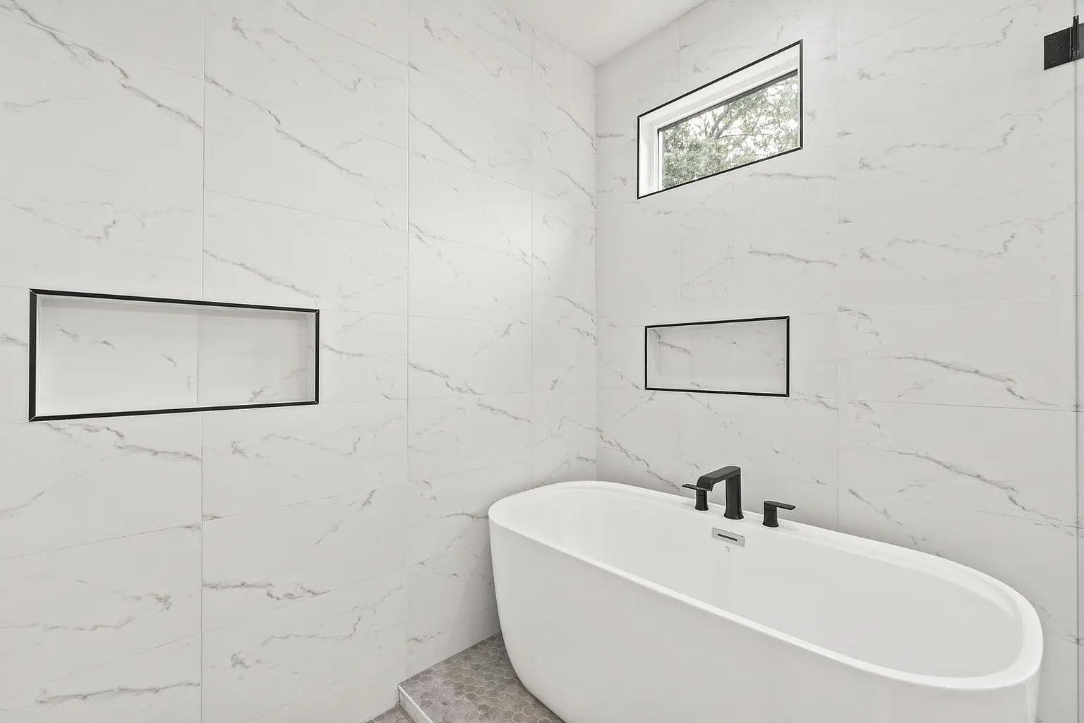 White bathroom with a bathtub, two recessed shelves, and a small window.