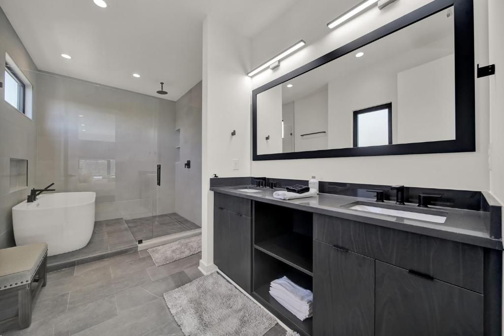 Modern bathroom with gray walls, black cabinetry, large mirror, shower, and freestanding tub.