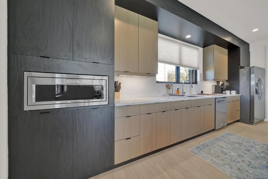 Modern kitchen with wooden cabinets, black accents, built-in oven, and stainless steel appliances.