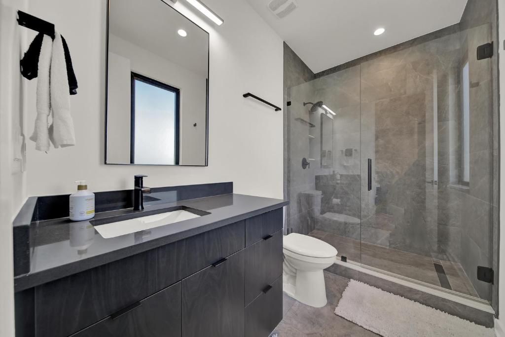 Modern bathroom with dark gray vanity, glass shower, and white toilet.