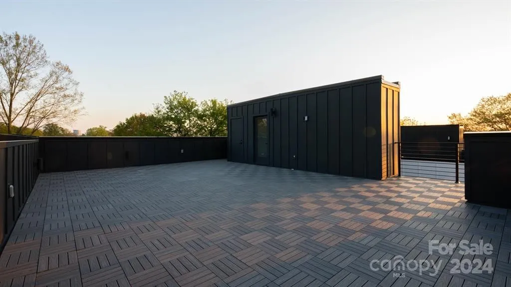 Rooftop deck with dark tiled floor, black structure, and surrounding trees. 