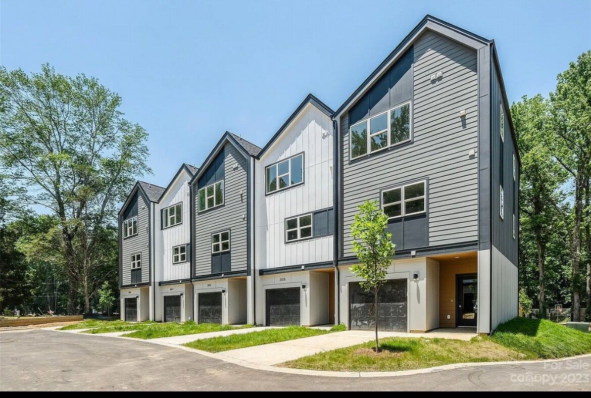 Modern townhomes with gray and white exteriors, black garage doors, and green grass in a sunny setting.