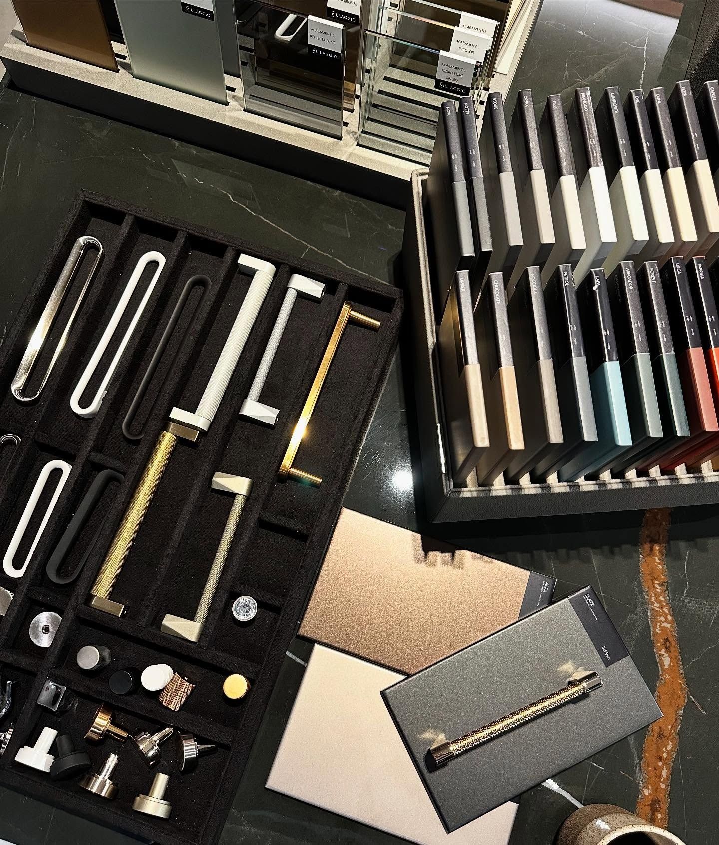 Display of cabinet hardware and tile samples. Silver, gold, and black pulls and knobs on black felt.