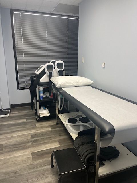 Examination room with treatment table, medical equipment, and a window with blinds.
