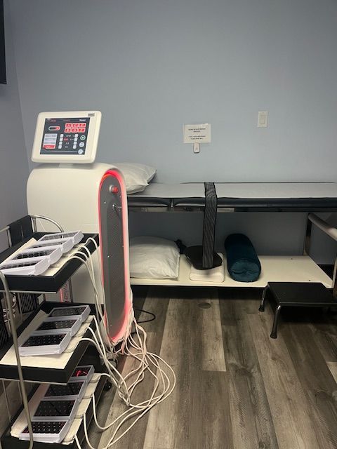 Medical exam room with a treatment table, equipment, and a screen, in front of a blue wall.