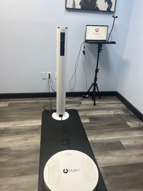 A white body composition scanner with laptop on tripod set up in a room with gray walls.