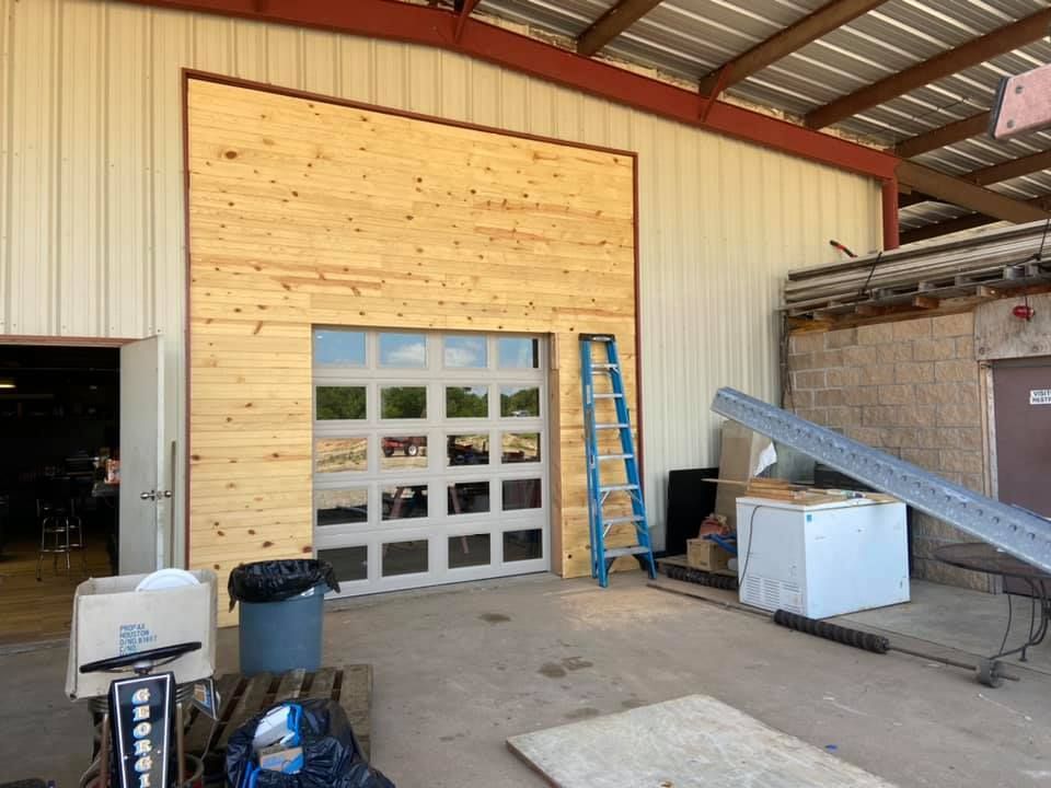 Garage exterior with a wooden facade around a glass door. A blue ladder and various items are nearby.