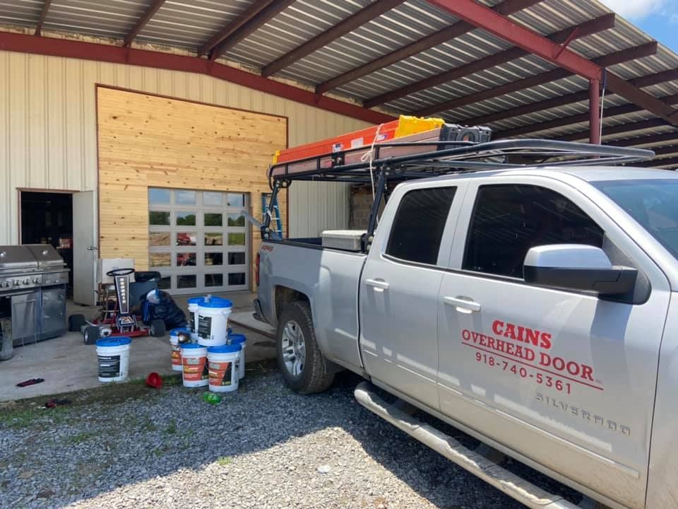 Silver truck parked in front of a building with a new glass garage door, next to buckets of paint.