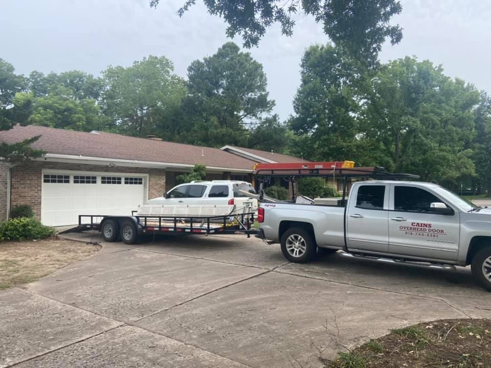 Silver truck towing a trailer with supplies parked in front of a house on a cloudy day.
