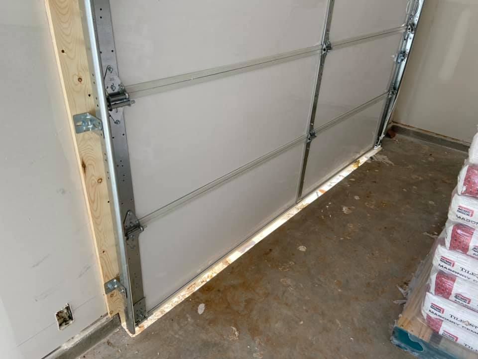 Garage door with white panels and metal framing, resting on a concrete floor.