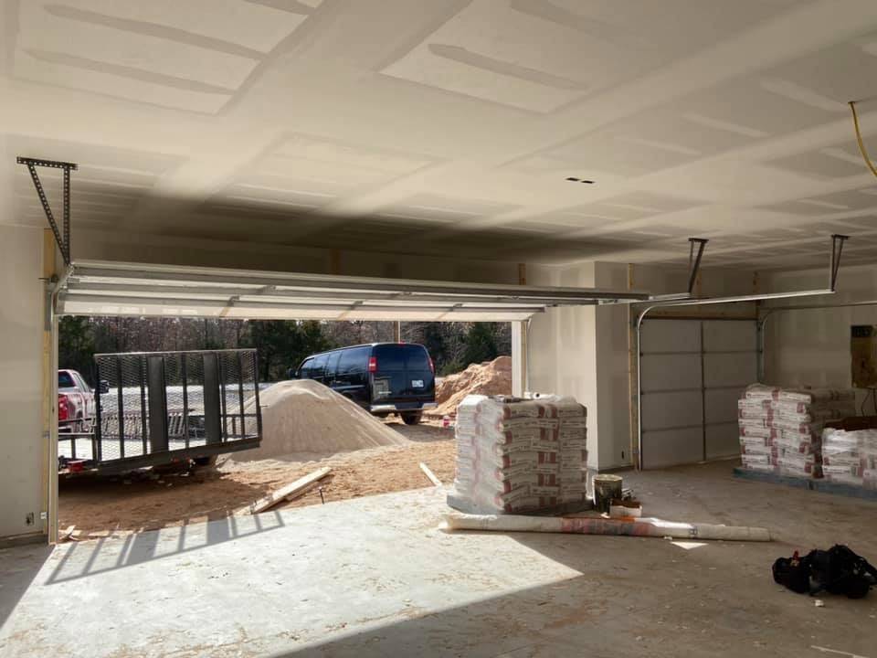 Garage interior under construction, door open to outside, trailer and materials visible.