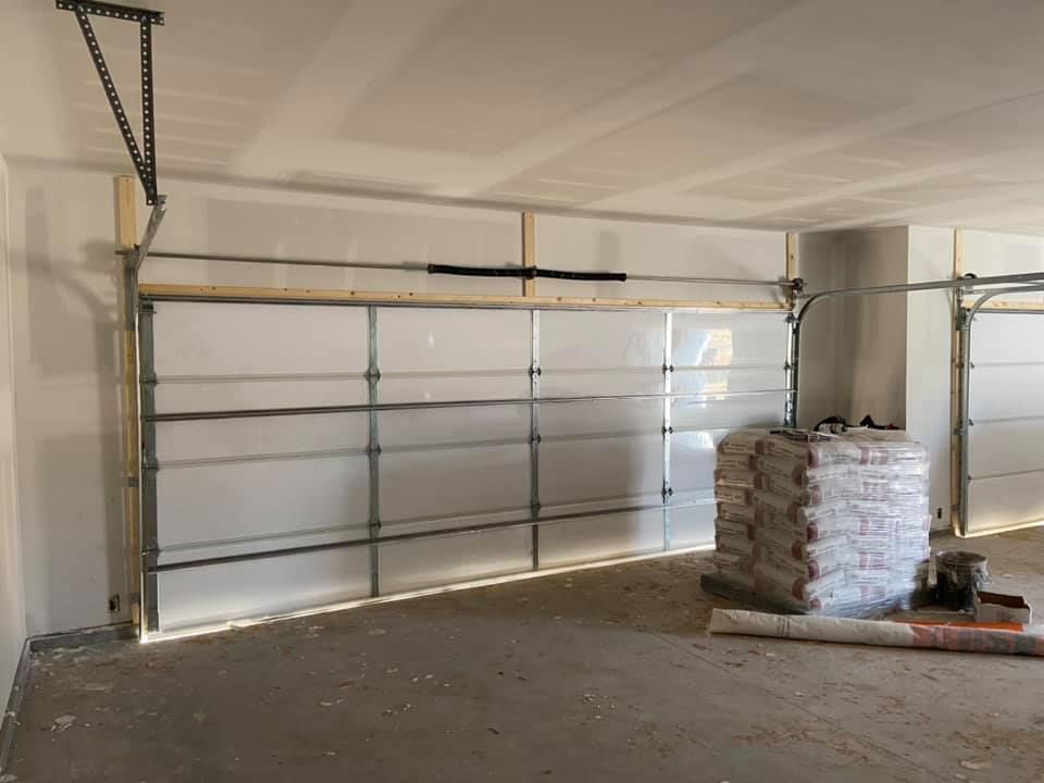 Garage interior with a partially installed garage door. There is a pile of bags in front of the door.