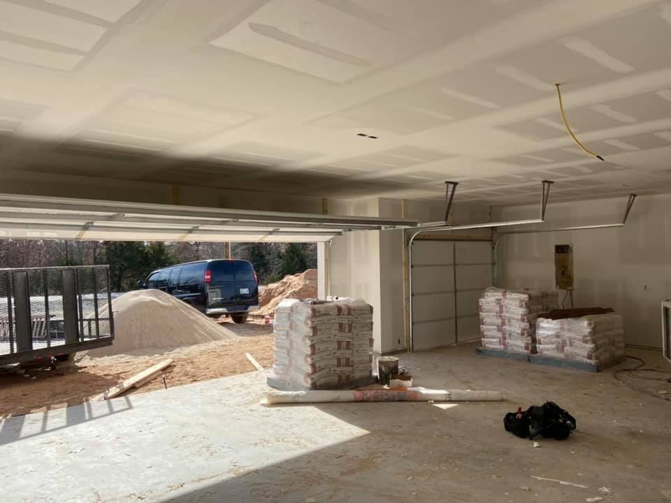 Interior of a garage under construction; drywall ceiling, open door, building materials, vehicle outside.