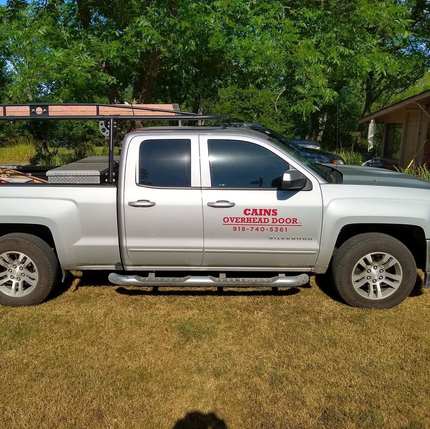 Silver pickup truck with CAINS OVERHEAD DOOR logo parked on grass.