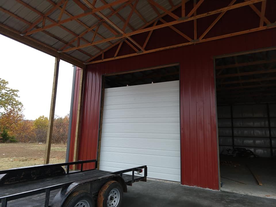 Red metal building with large white garage door, open. Trailer parked in front.