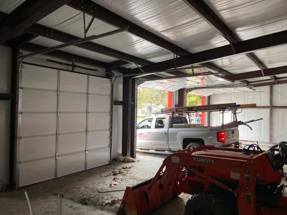 Garage with open door, a truck entering, and an orange tractor in front. Interior view.