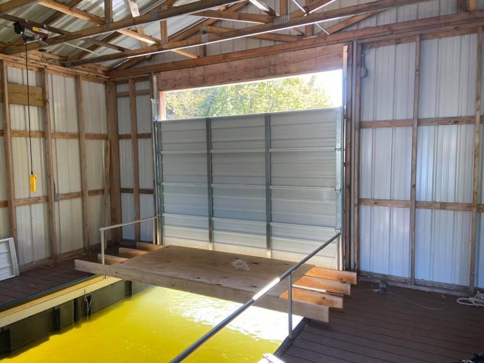 Boat dock with a metal door and wooden ramp leading to the water, inside a wooden and metal structure.
