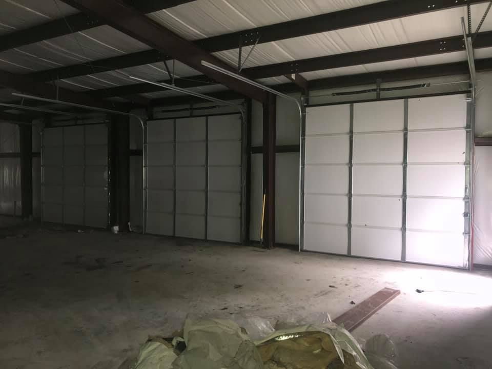 Interior of an empty warehouse with three closed garage doors. Metal beams support the roof.