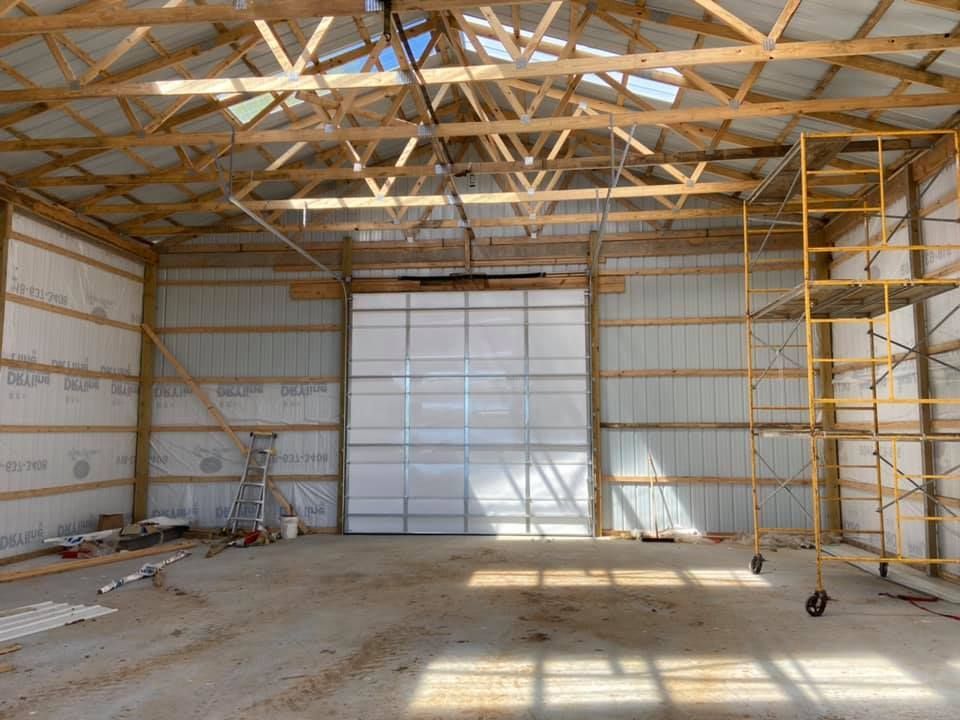 Interior of a partially constructed metal building with large overhead door, scaffolding, and wood framing.