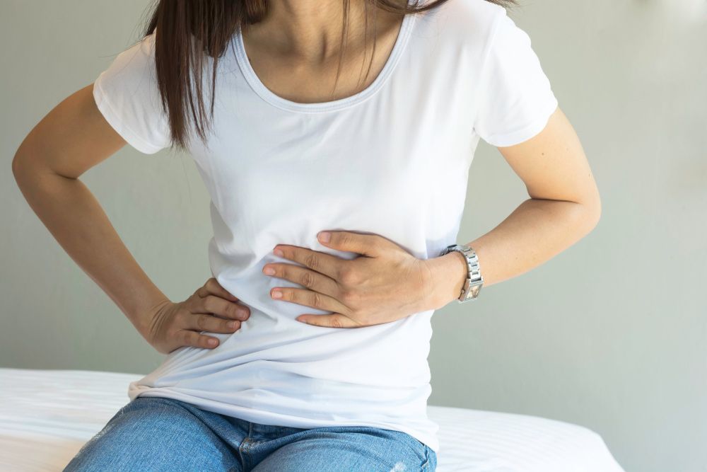 A Woman is Sitting on a Bed With Her Hands on Her Stomach — Brisbane Upper GI Surgery in Chermside, QLD