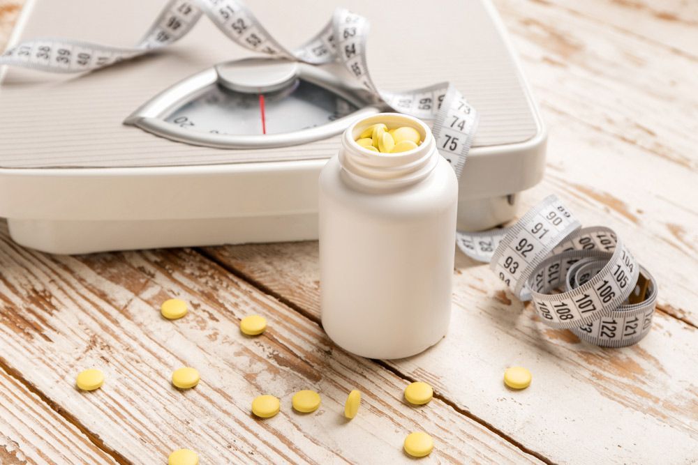 A Bottle of Pills Next to a Scale and Measuring Tape on a Wooden Table — Brisbane Upper GI Surgery in Chermside, QLD