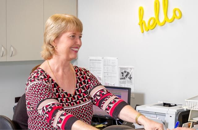 A Woman is Sitting at a Desk in Front of a Wall That Says Hello — Brisbane Upper GI Surgery in Chermside, QLD