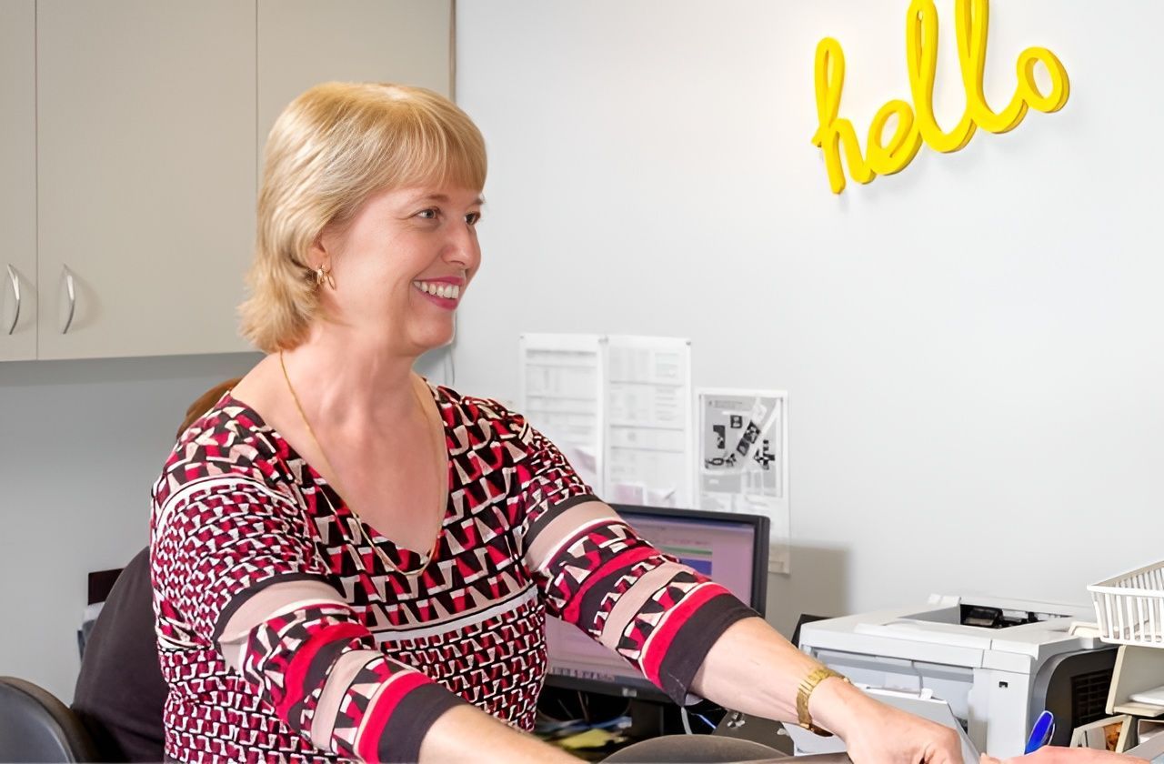 A Woman is Sitting at a Desk in Front of a Wall That Says Hello — Brisbane Upper GI Surgery in Chermside, QLD