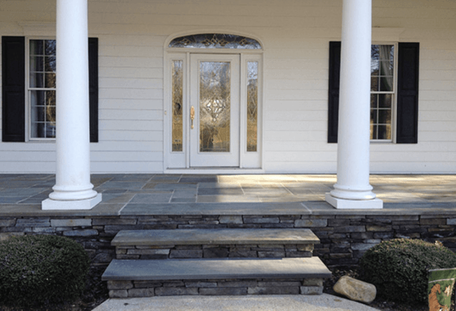 A white house with black shutters and a stone porch