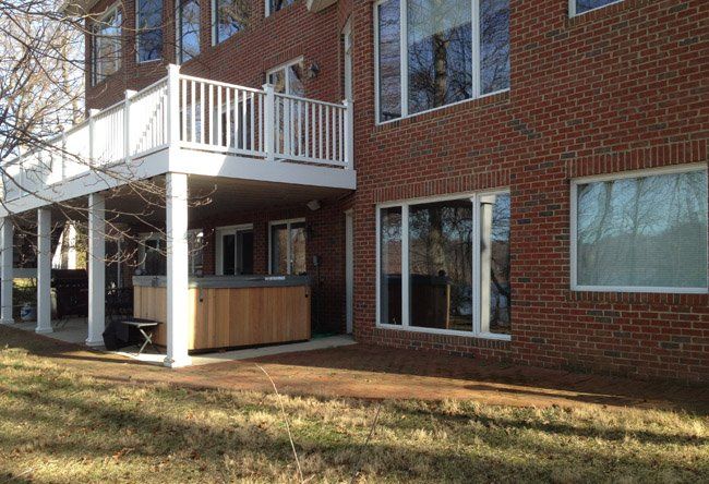 A large brick house with a large deck and a hot tub underneath it.