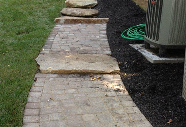 A stone walkway leading to a house with a green hose.