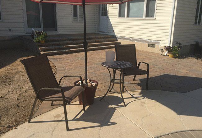 Two chairs and a table under an umbrella on a patio in back of a house.