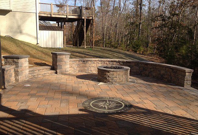 There is a fire pit in the middle of the patio with a retaining wall.