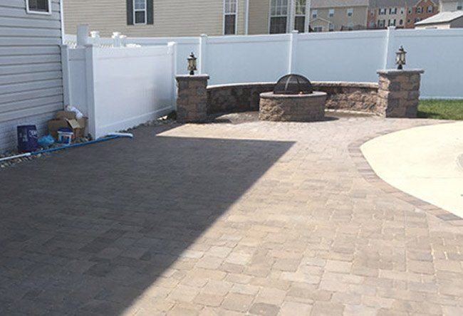 A patio with a fire pit and a white fence