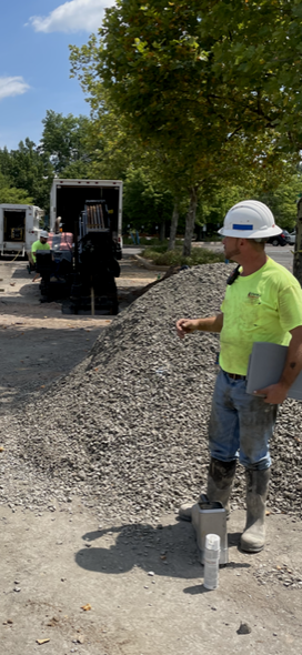 A man in a hard hat is standing in the dirt holding a shovel.