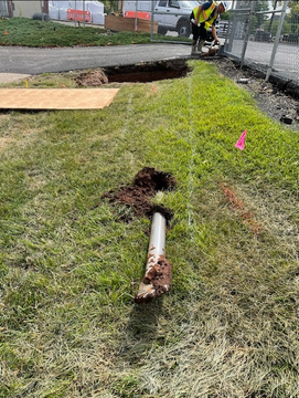 A man is digging a hole in the grass next to a drain pipe.