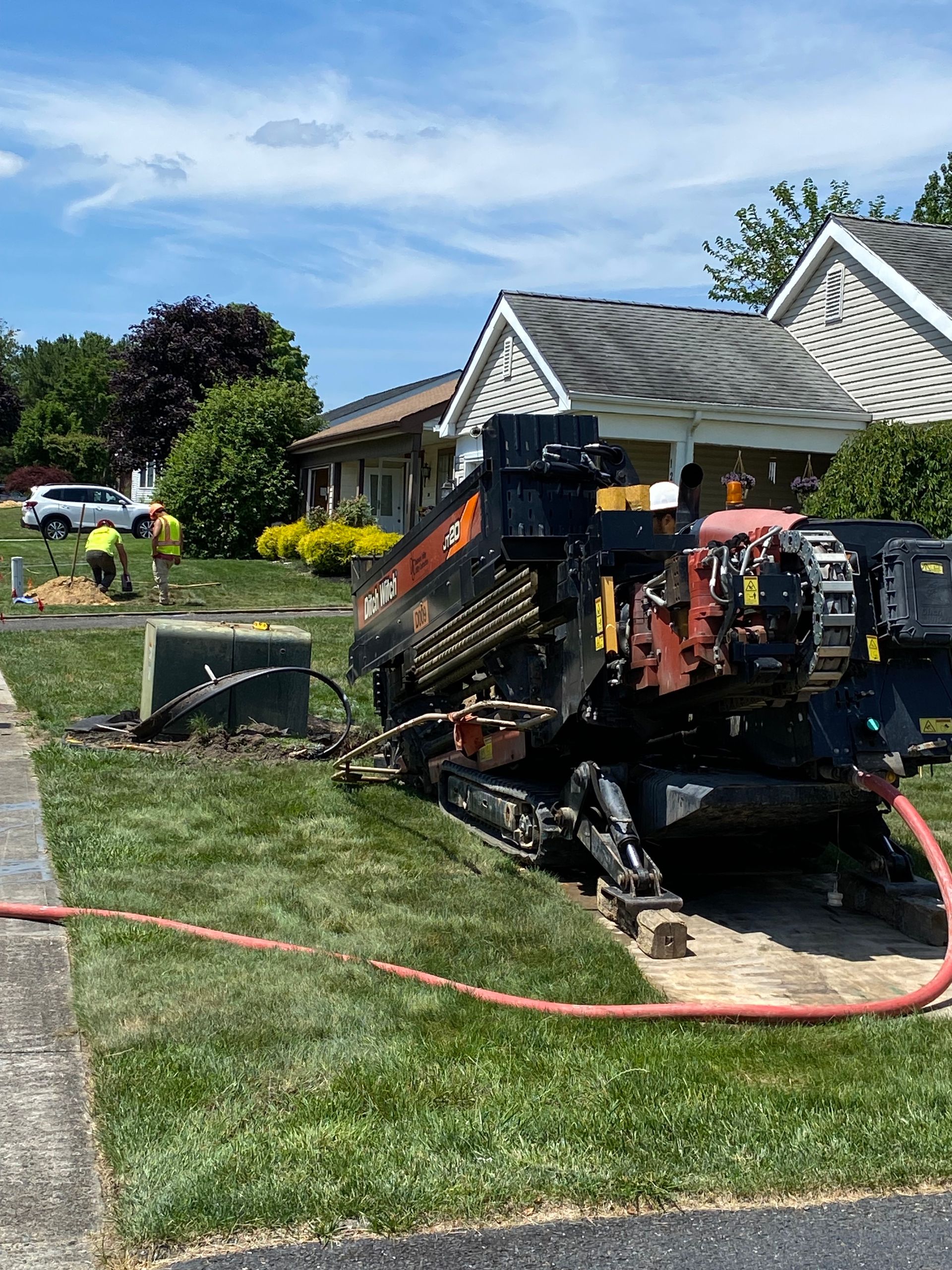 A hdd drill is sitting in the grass in front of a house.