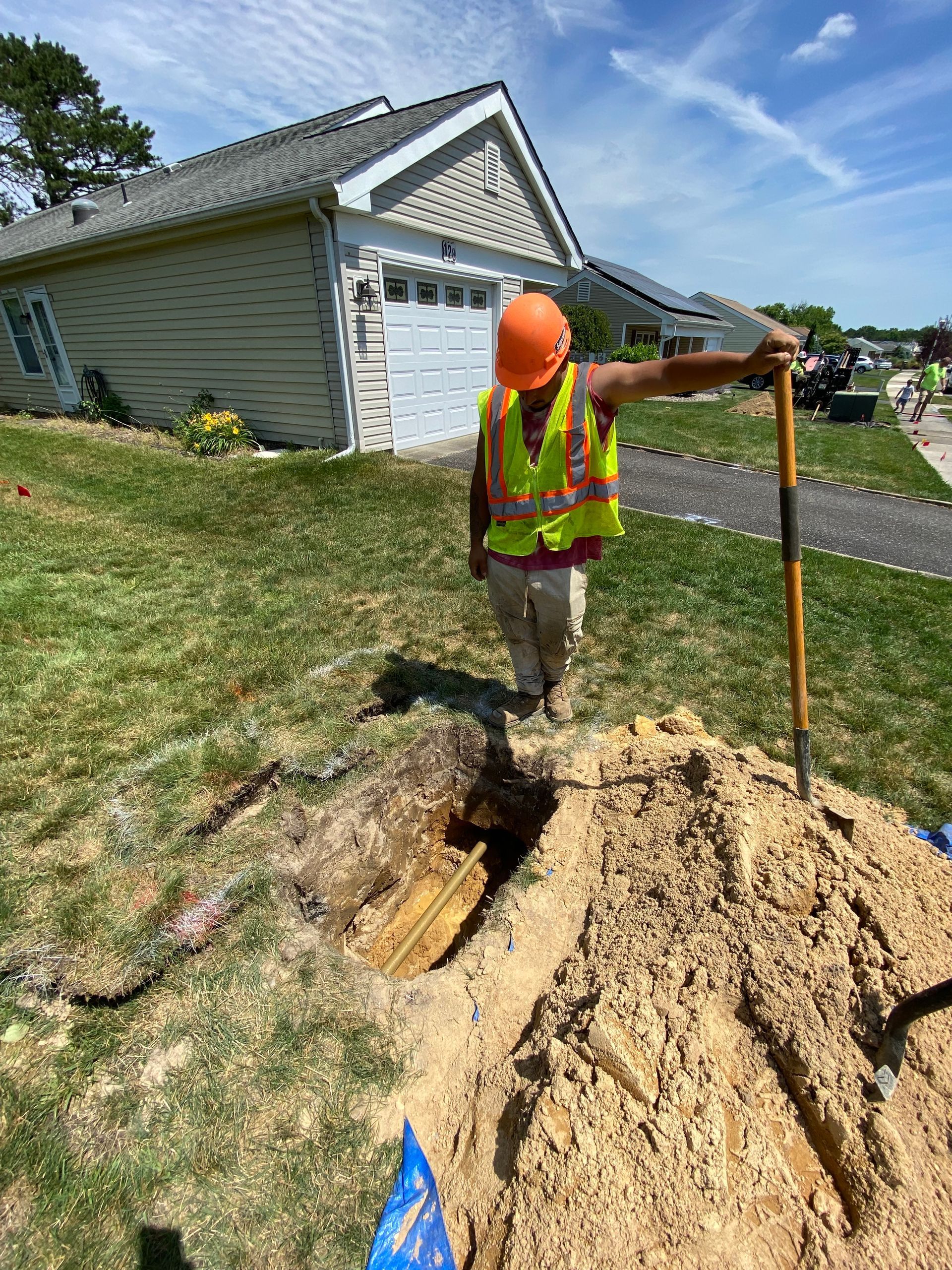 A construction worker is digging a hole in the ground in front of a house.