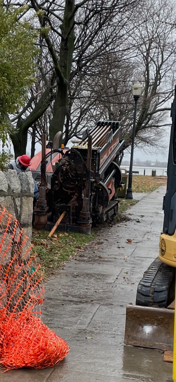 A construction vehicle is sitting on the sidewalk next to a fence.