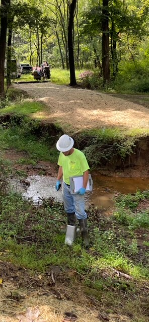 A man is standing next to a stream in the woods.